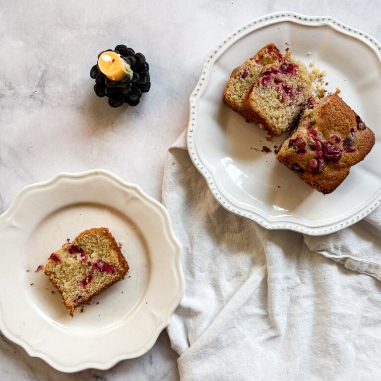 A candle burns next to slices of gluten free cranberry lemon loaf.
