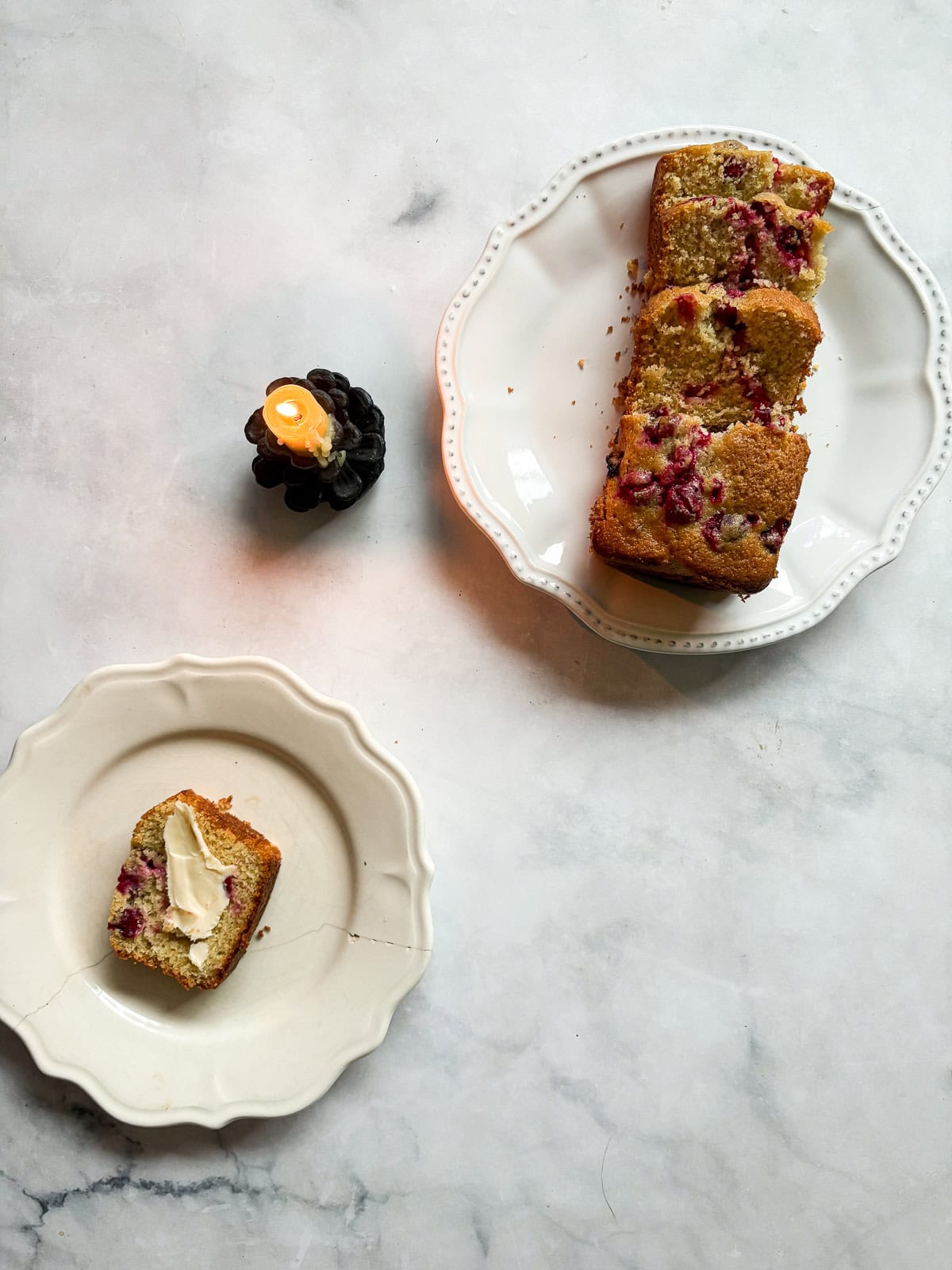 Perfect for holiday baking, this gorgeous gluten free cranberry lemon bread is studded with tart, juicy pops of cranberries. A candle burns next to slices of gluten free cranberry lemon loaf.