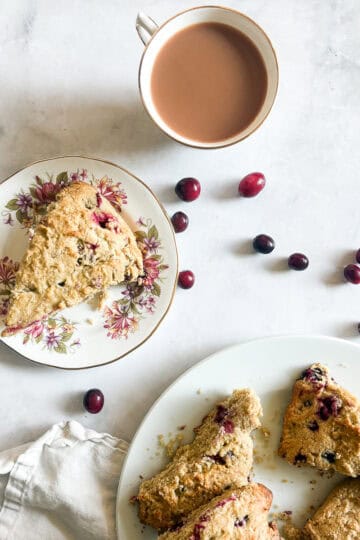 Cranberries are scattered around plates of gluten free cranberry scones.