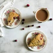 Fresh cranberries are scattered around plates of gluten free cranberry scones.