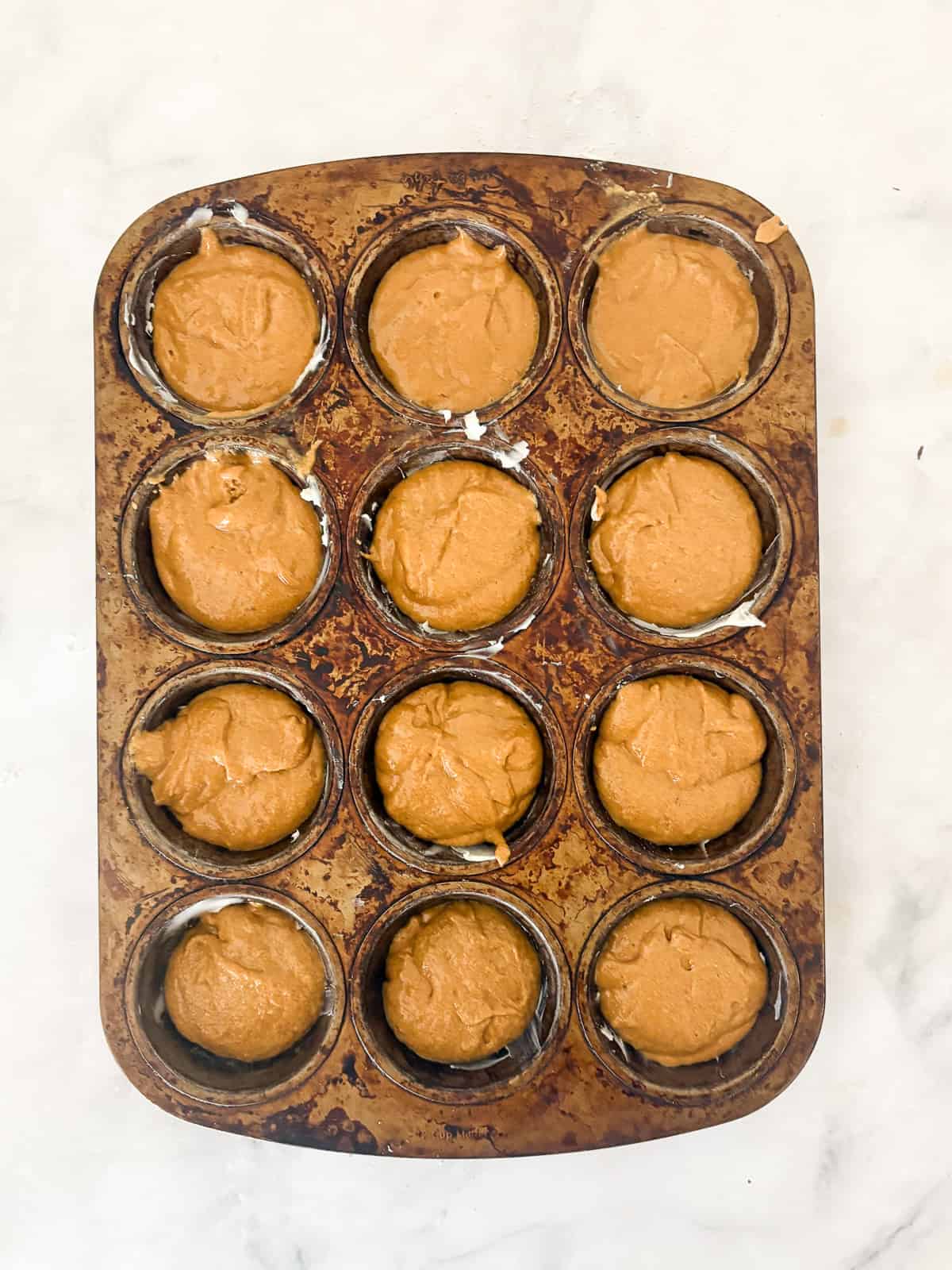 Warmly spiced gluten-free gingerbread muffins take everything you love about classic gingerbread and turn it into a handheld snack! Gluten free gingerbread muffin batter in a muffin tin.
