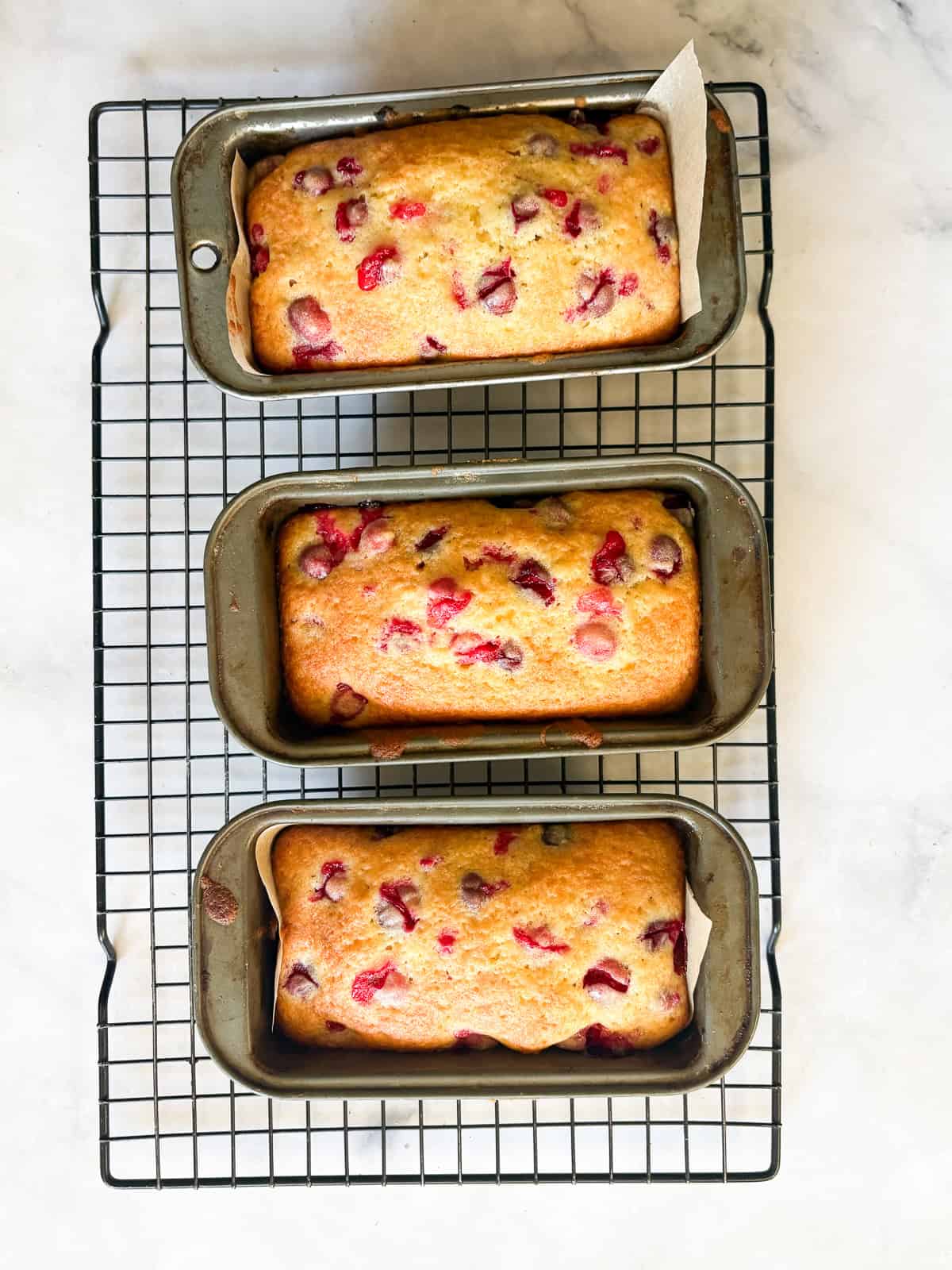 Perfect for holiday baking, this gorgeous gluten free cranberry lemon bread is studded with tart, juicy pops of cranberries. Baked loaves of gluten free cranberry lemon bread cool on a rack.
