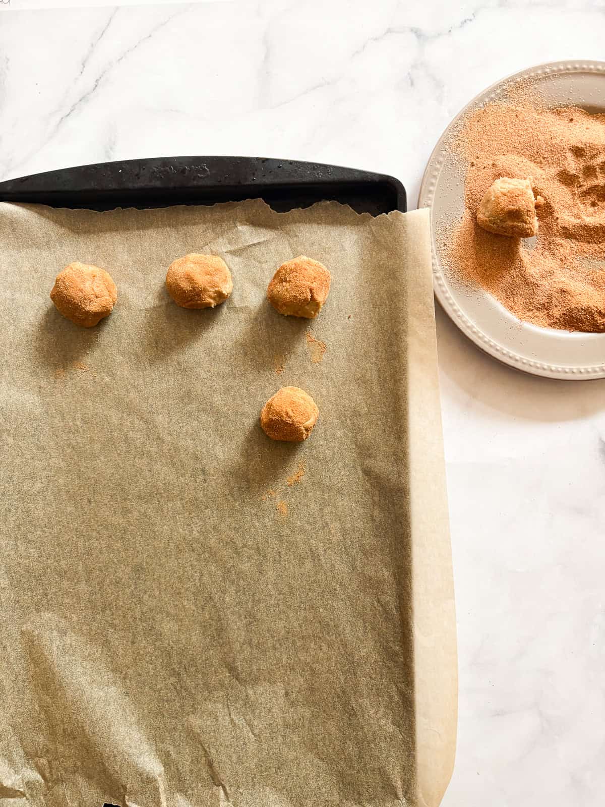 Balls of gluten free snickerdoodles dough on a baking sheet.