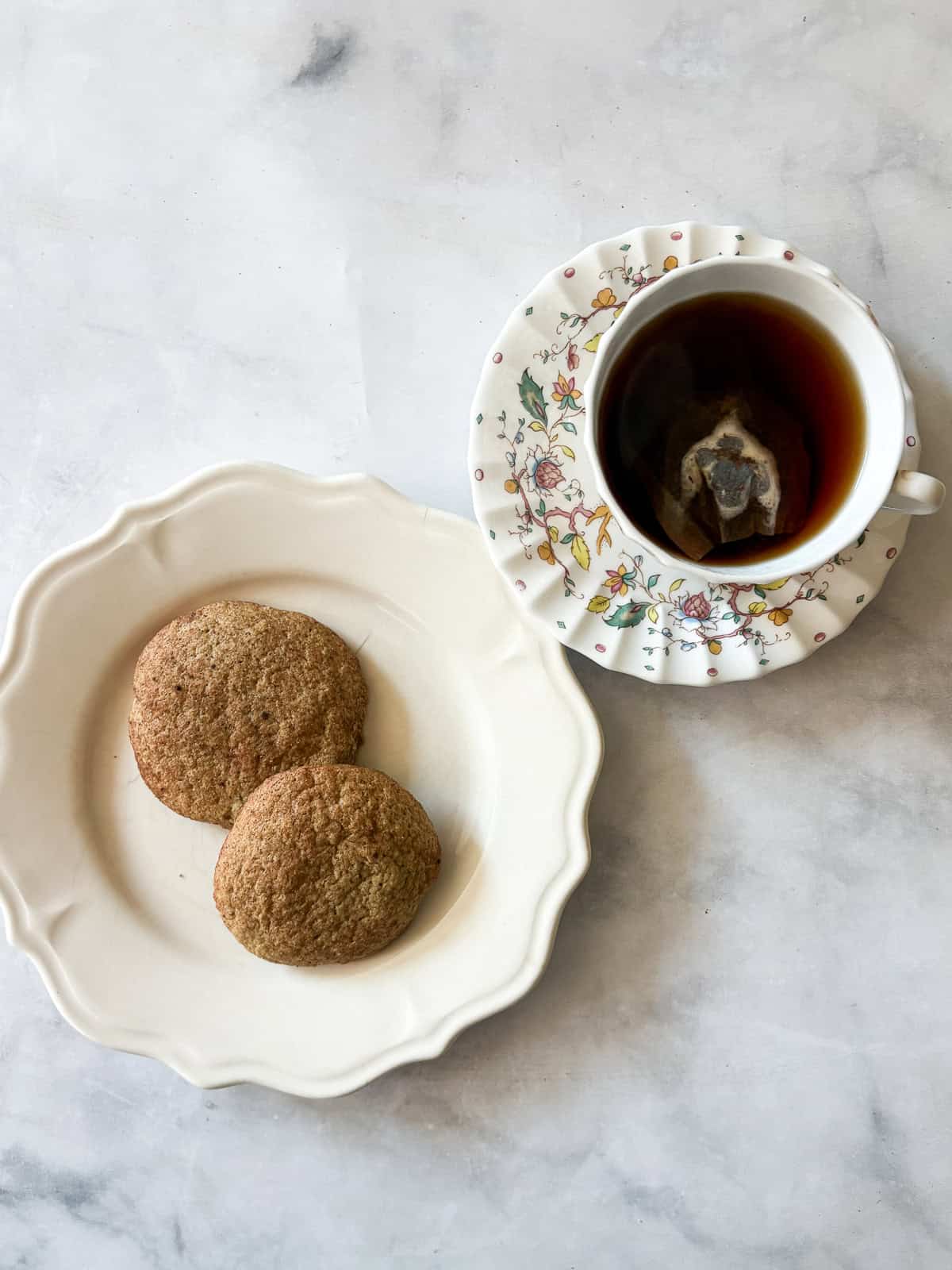 Two gluten free snickerdoodle cookies on a plate next to a cup of tea.