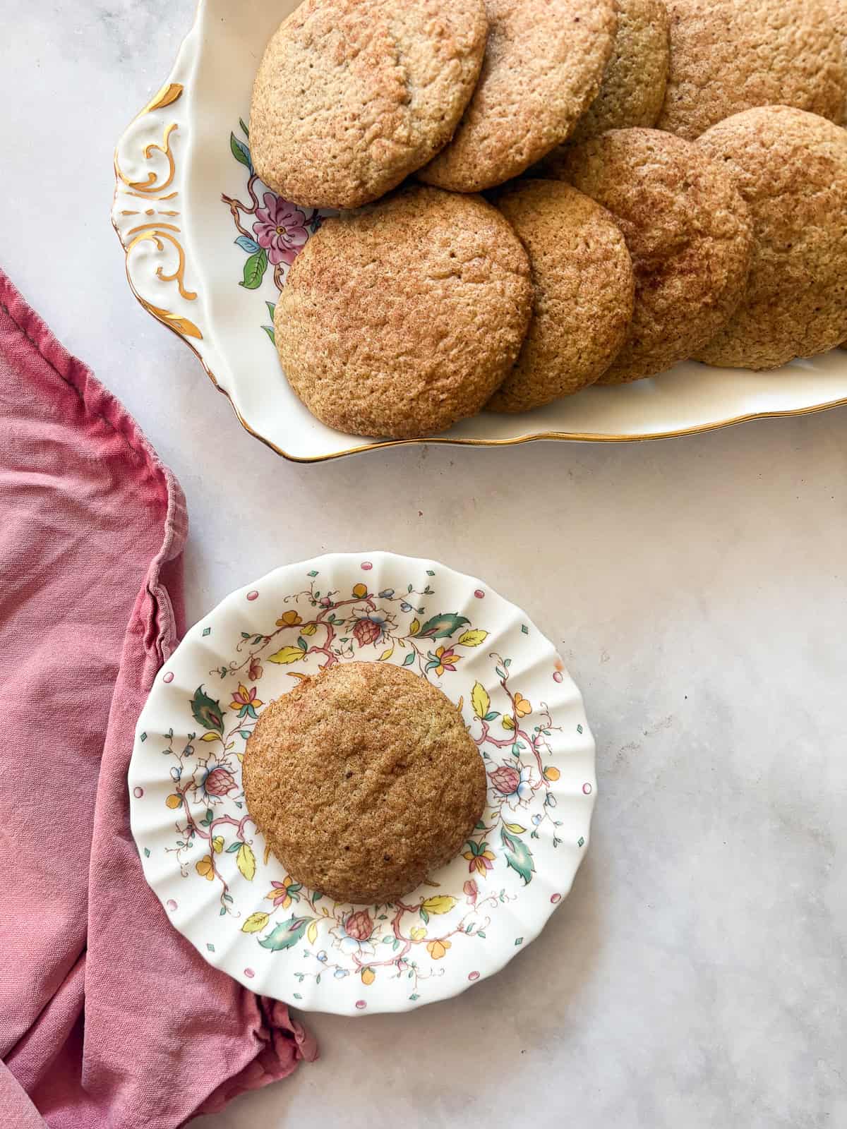A gluten free snickerdoodle cookie on a plate next to more cookies.