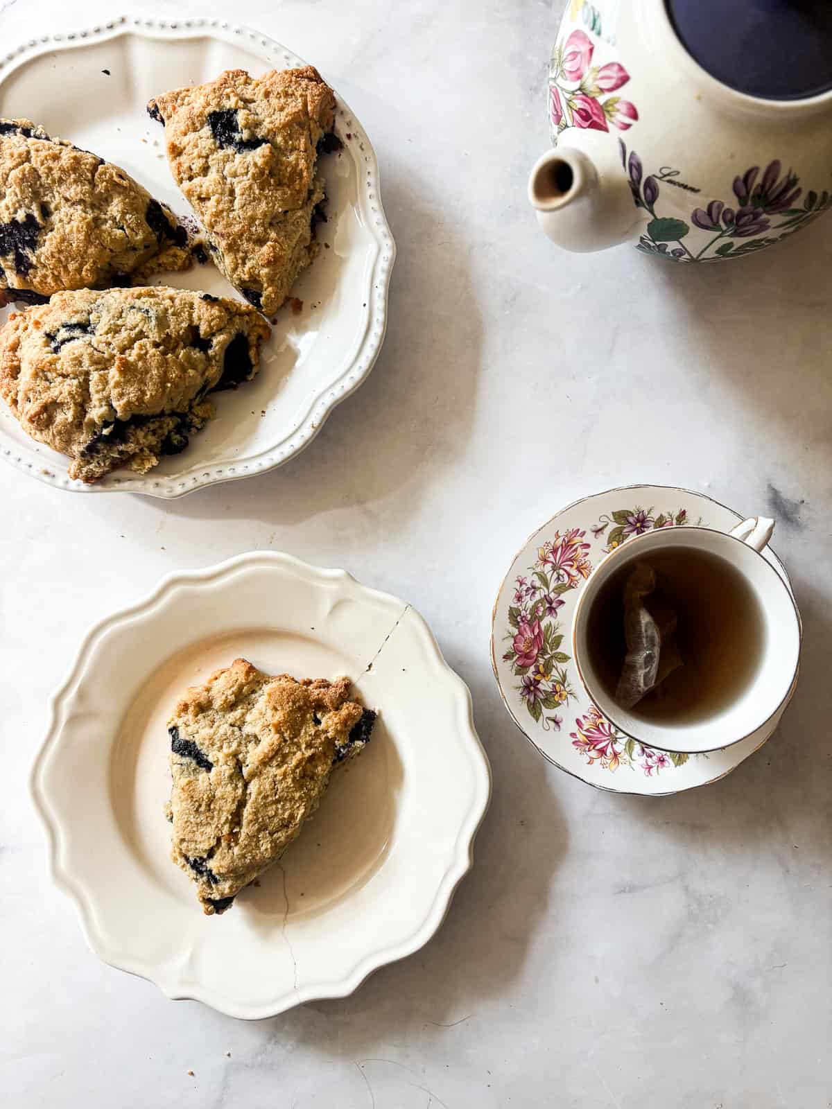 A berry buckwheat scone on a plate with a pot of tea.