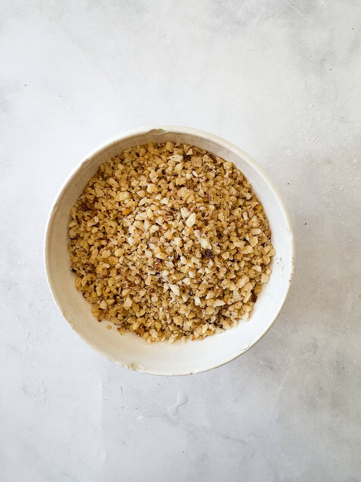 Chewy Moroccan ghriba cookies with walnuts and cinnamon are lightly sweet, rolled in powdered sugar, and easily gluten-free. Ground walnuts in a bowl.