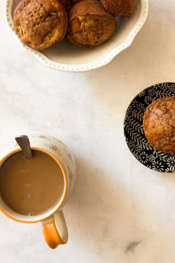 A bowl of gluten free apple banana bread muffins and a cup of coffee.