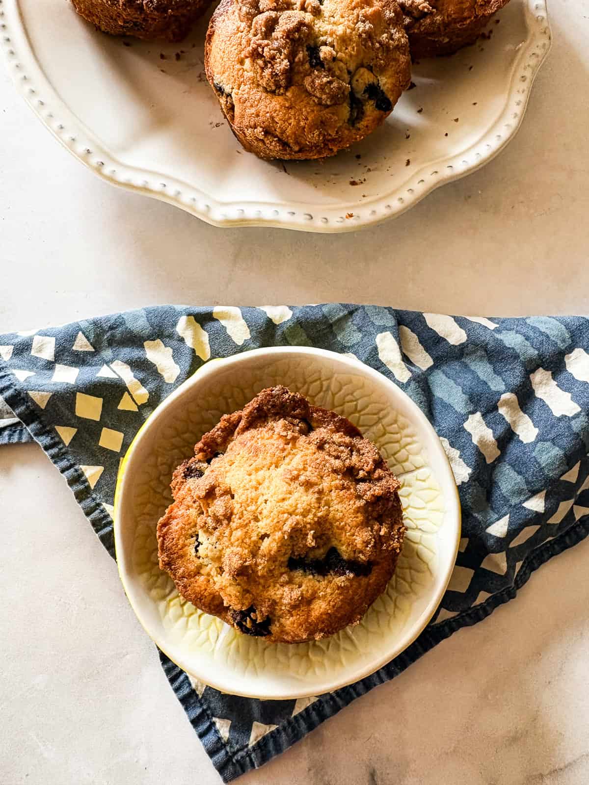 A gluten-free bakery-style blueberry muffin on a plate with a blue napkin.