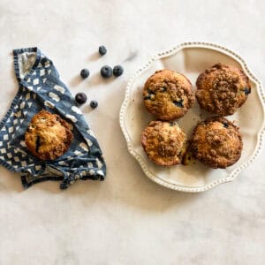 Gluten-free bakery-style blueberry muffins with blueberries scattered around them.