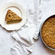 A fork cuts into a slice of chocolate chip cookie cake, with the pan of cake and a napkin next to it.