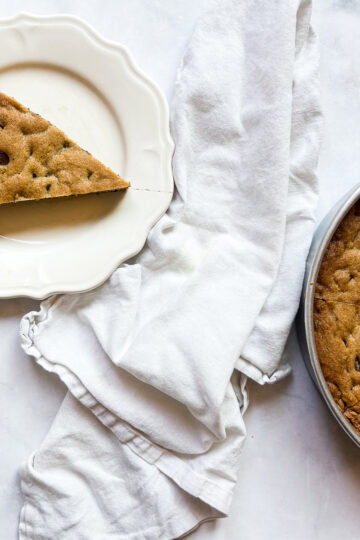 A fork cuts into a slice of chocolate chip cookie cake, with the pan of cake and a napkin next to it.