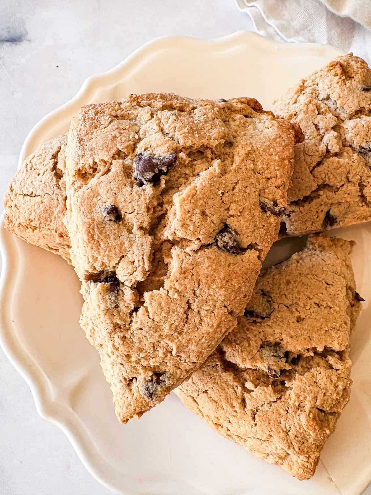 Bakery-style gluten-free chocolate chip scones with crisp edges, soft centers, and plenty of chocolate. Made just with oat flour! Chocolate chips peek out of a gluten free chocolate chip scone on top of more scones.