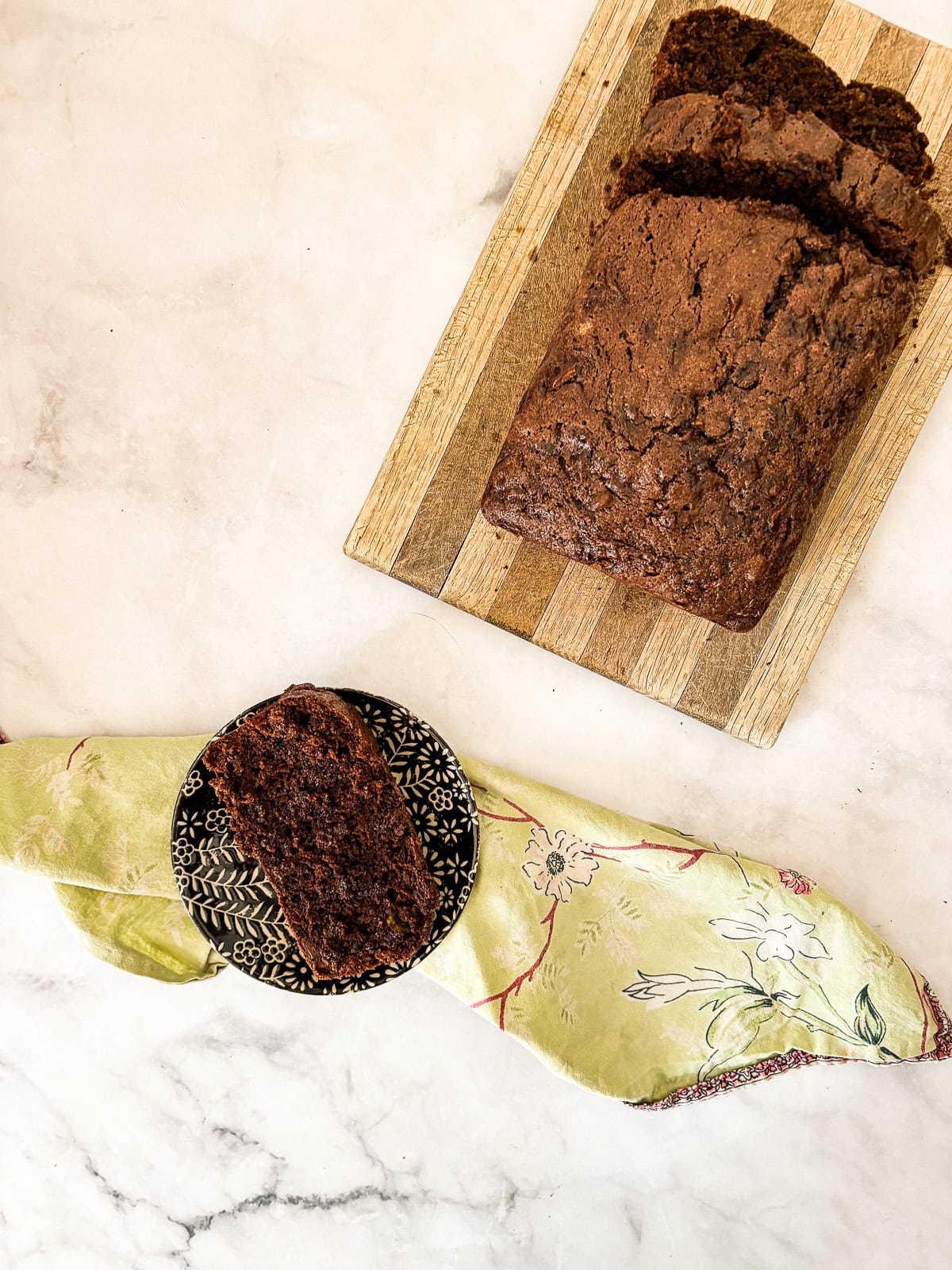 A slice of gluten free chocolate zucchini bread on a plate next to the sliced loaf.