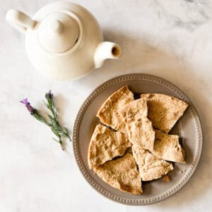 A white tea pot next to a plate of gluten free lavender shortbread cookies and a few sprigs of lavender.