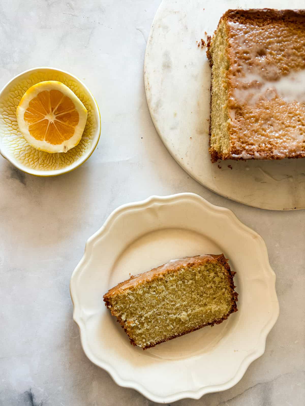 This rich and velvety gluten free lemon pound cake stays moist and tender for days! Made with oat and almond flour, cream cheese, and butter! A slice of gluten free lemon pound cake on a plate with half a lemon next to it.