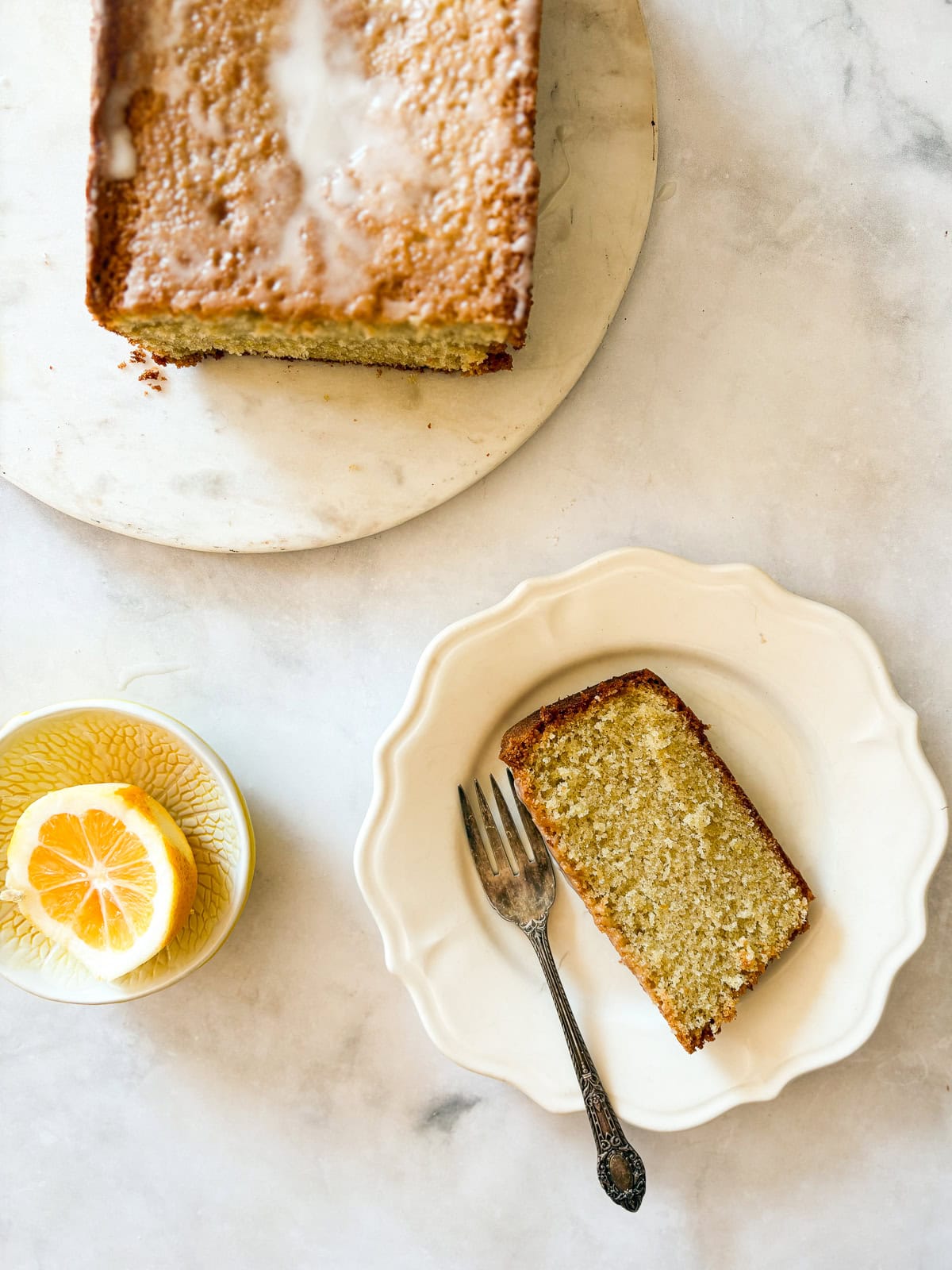 A slice of gluten free lemon pound cake on a plate with a fork next to the loaf.