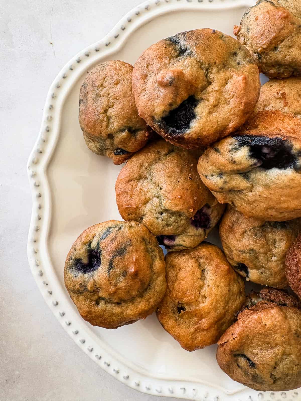 Two-bite, gluten-free mini blueberry muffins are made with whole-grain oat flour, Greek yogurt, and plenty of juicy berries. Kids love them! Gluten free mini blueberry muffins piled on a plate.