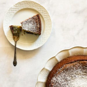A fork cuts into a piece of gluten free poppyseed cake on a plate next to the cake.