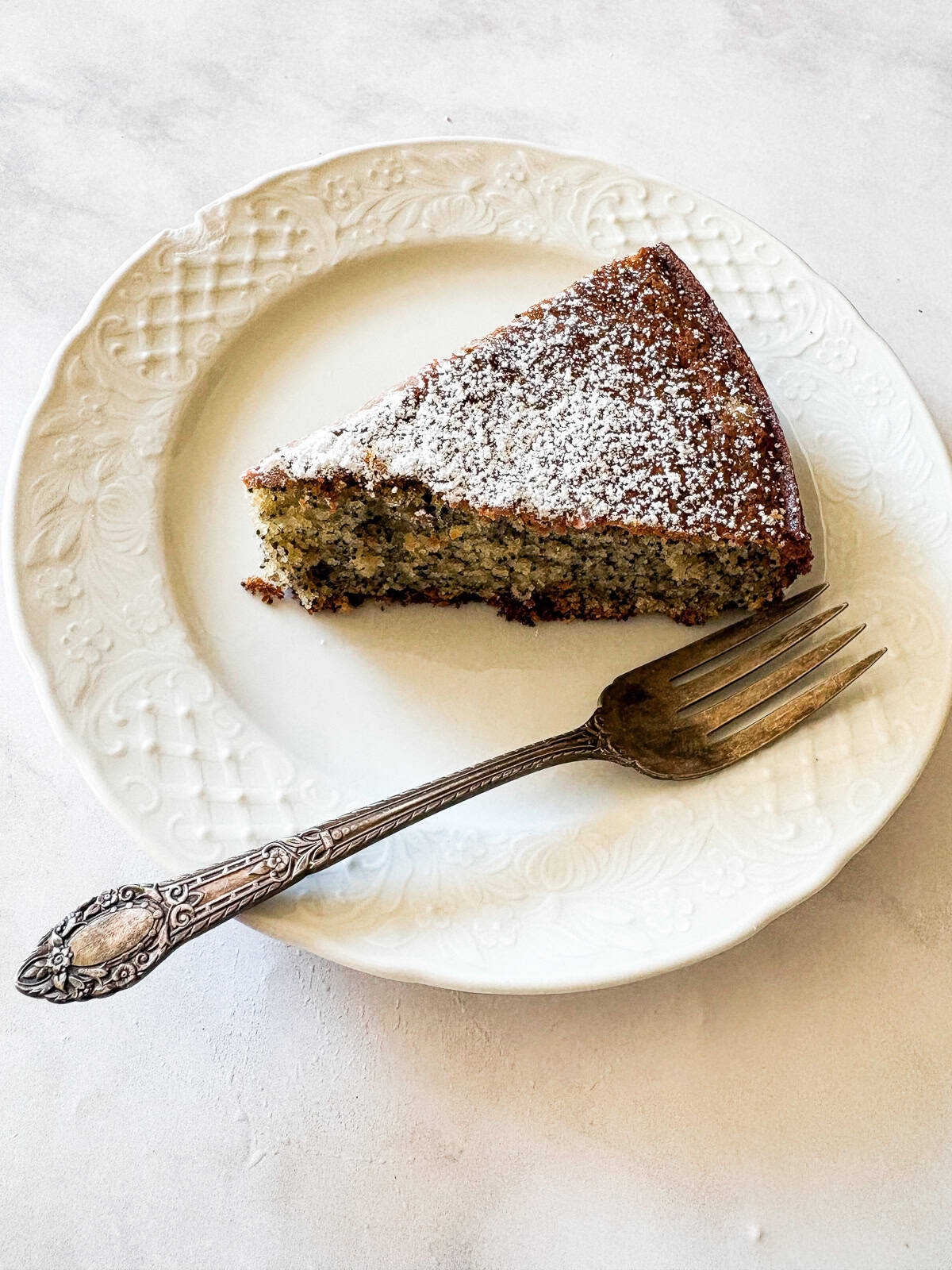 his gluten-free poppyseed cake is tender-crumbed, generously speckled with poppyseeds, and made with two simple flours. A slice of gluten free poppyseed cake on a plate with a fork.