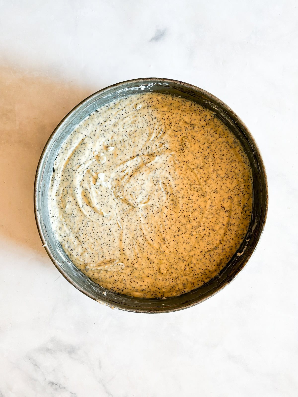 his gluten-free poppyseed cake is tender-crumbed, generously speckled with poppyseeds, and made with two simple flours. Poppyseeds added to gluten free poppyseed cake batter in a cake pan.