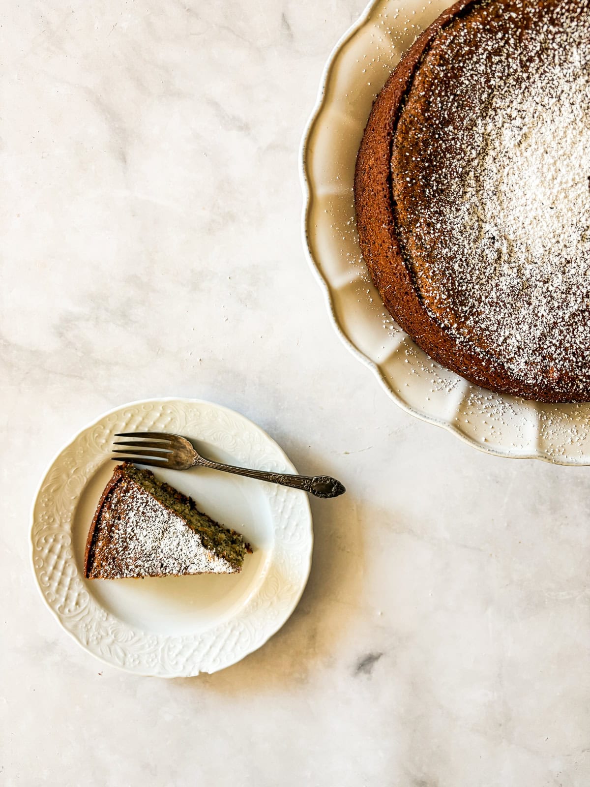 A slice of gluten free poppyseed cake on a plate next to the cake.