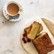 Berries surround a gluten-free pound cake next to a cup of tea.