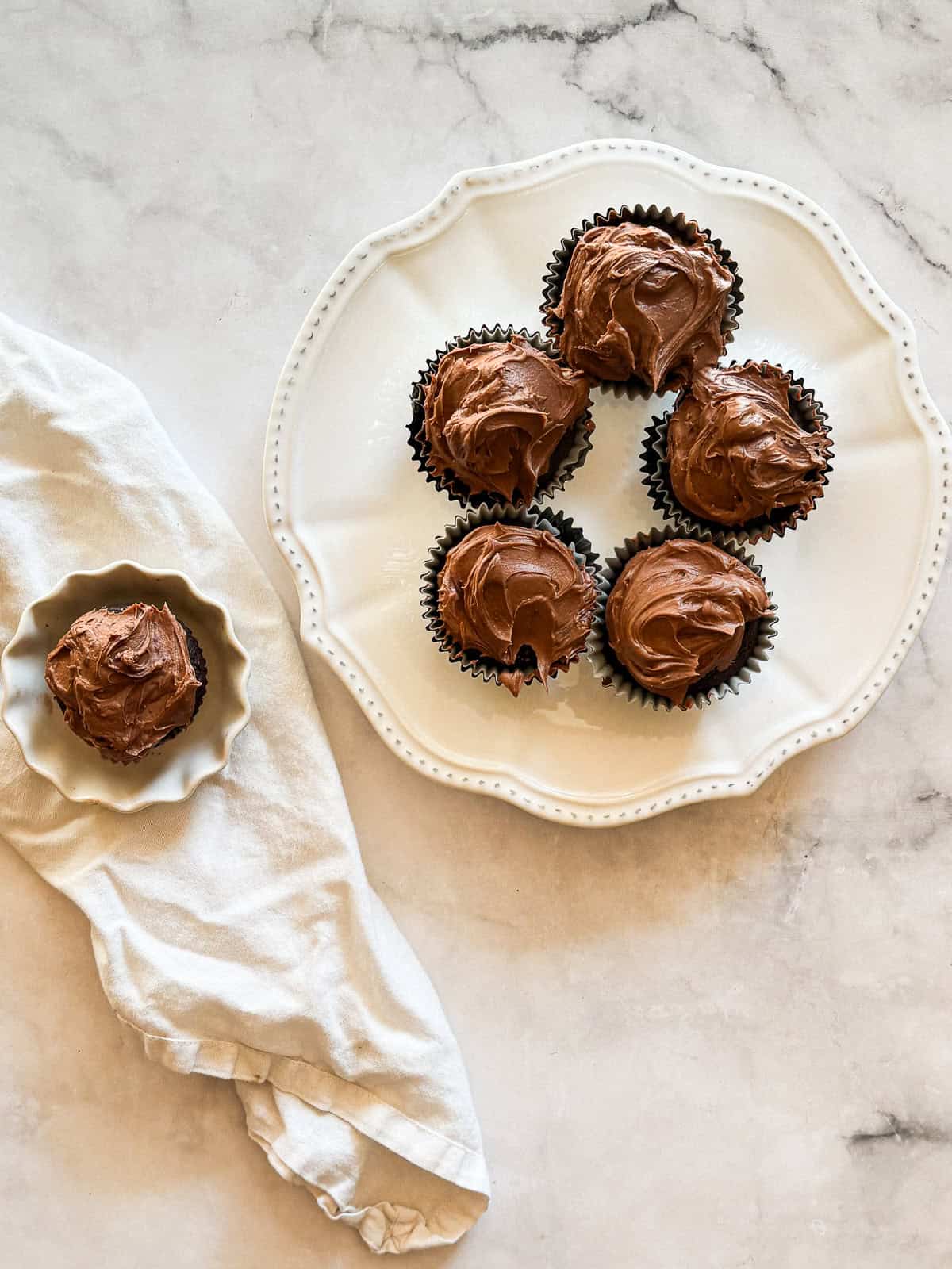 A plate of vegan gluten-free chocolate cupcakes and a cupcake on a napkin.