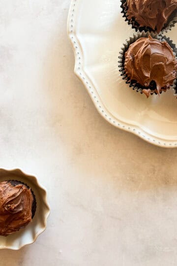 A vegan gluten-free chocolate cupcakes in a little bowl next to a plate of cupcakes.