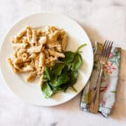 A plate of gluten free baked mac and cheese with spinach and a fork and napkin.