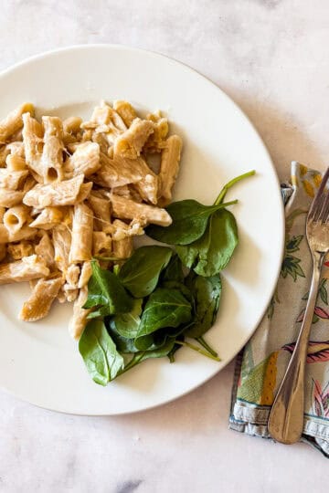 A plate of gluten free baked mac and cheese with spinach and a fork and napkin.