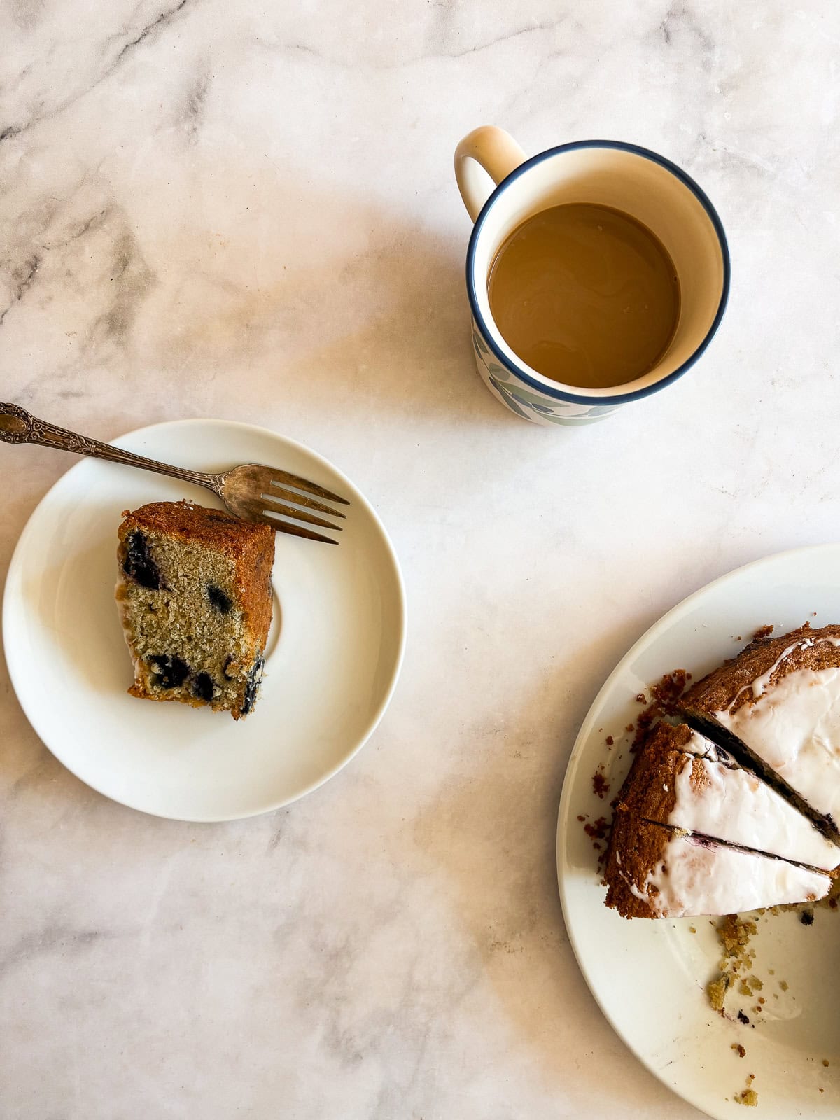 A rich and fluffy gluten free blueberry cake that's packed with loads of juicyberries - you'll taste them in every bite! A slice of gluten free blueberry cake on a plate with a cup of coffee and more cake.