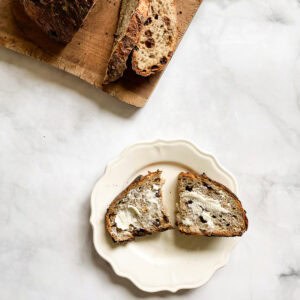 A loaf of gluten free cinnamon raisin bread on a cutting board and a slice of bread on a plate.