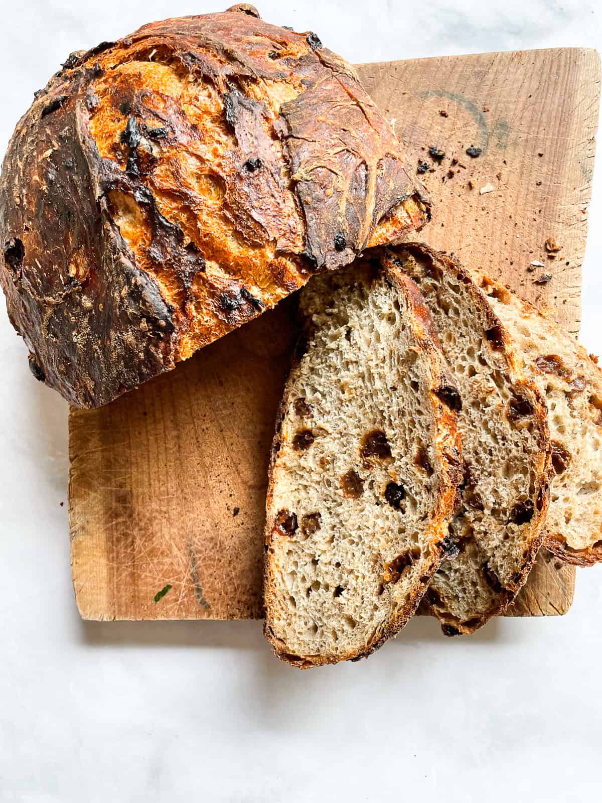 Easy no knead gluten free cinnamon raisin bread benefits from a long overnight rise and a bake in a hot Dutch oven. A loaf of gluten free cinnamon raisin bread on a wooden cutting board, with slices cut from it.
