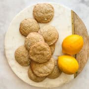 A couple of lemons and a bunch of gluten free lemon cookies on a plate.