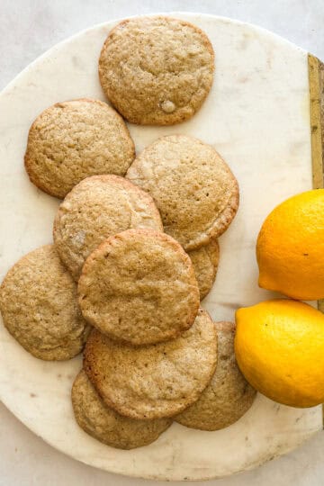 A couple of lemons and a bunch of gluten free lemon cookies on a plate.