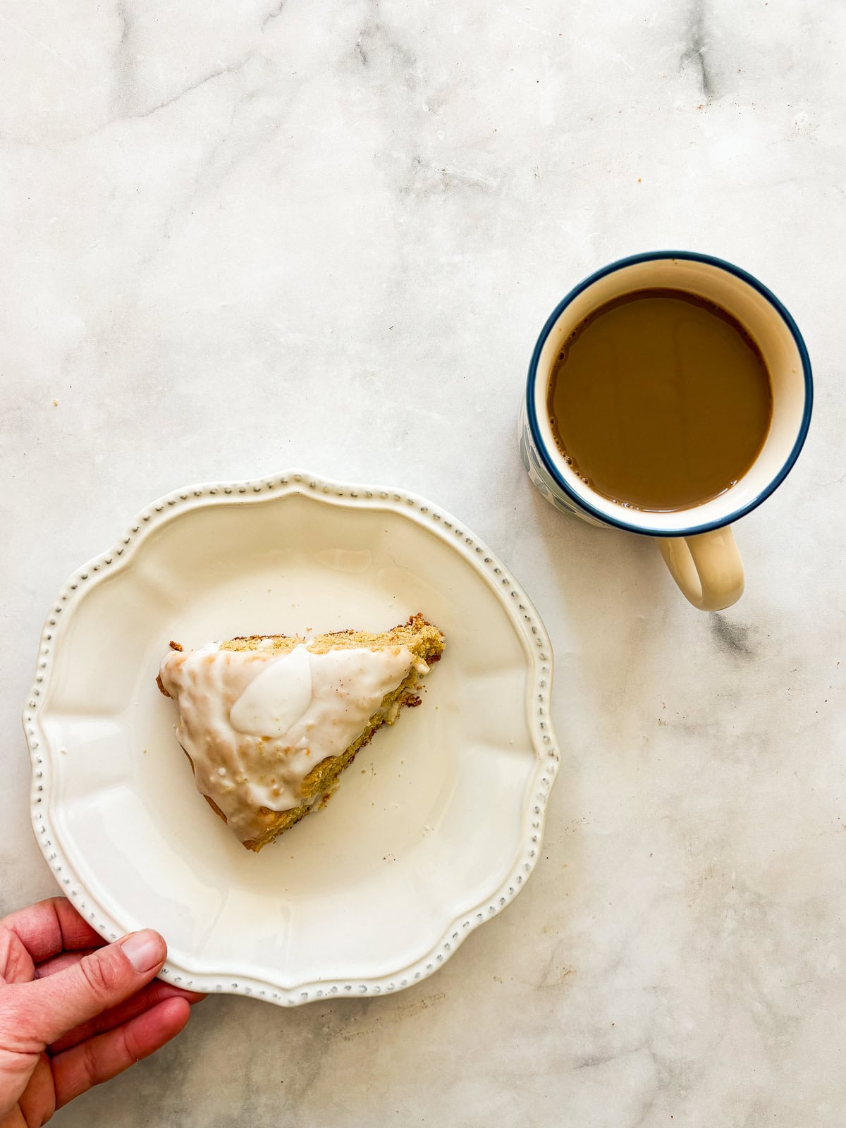 A simple recipe for gluten free lemon scones that tucks lots of fresh lemon zest into a tender, flaky oat flour scone topped with lemon glaze. A hand moves a plate with a gluten free lemon scone.