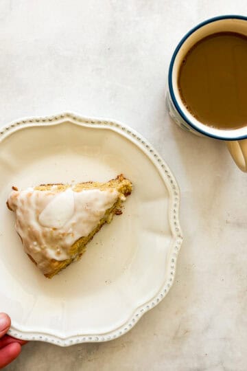 A hand moves a plate with a gluten free lemon scone.