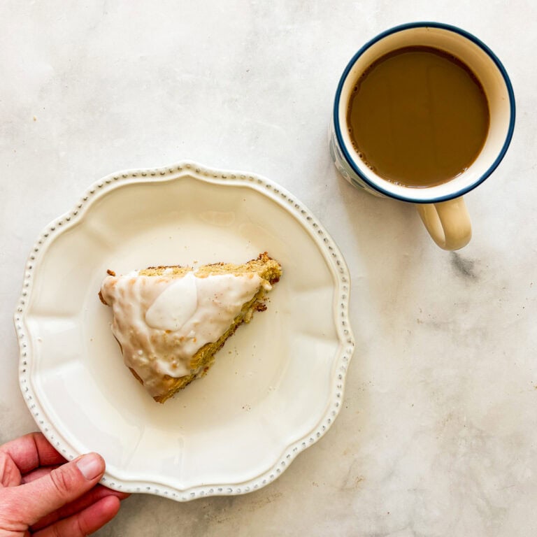 A hand moves a plate with a gluten free lemon scone.
