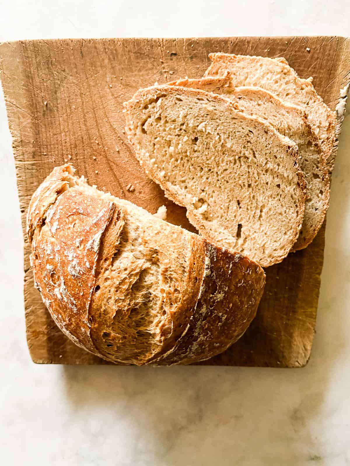 Easy dutch oven bread is my version of the beloved no knead bread recipe. Made with 4 ingredients and baked to golden perfection. A loaf of gluten free no knead bread on a cutting board with slices cut.