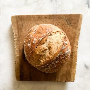 A loaf of gluten free no knead bread on a wooden cutting board.