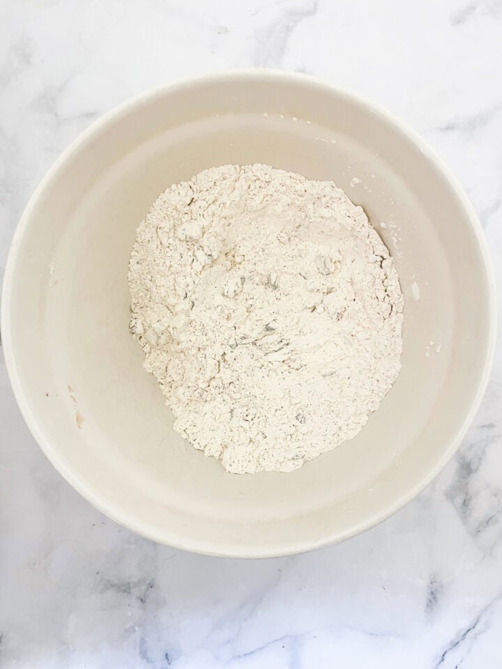 This rustic no-knead gluten free cranberry and walnut bread is jam-packed with extras and features a beautiful, gluten-free crumb. The dry ingredients for gluten free no knead cranberry bread are mixed in a bowl.