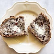 A slice of gluten free no knead cranberry walnut bread cut in half and spread with butter on a plate.