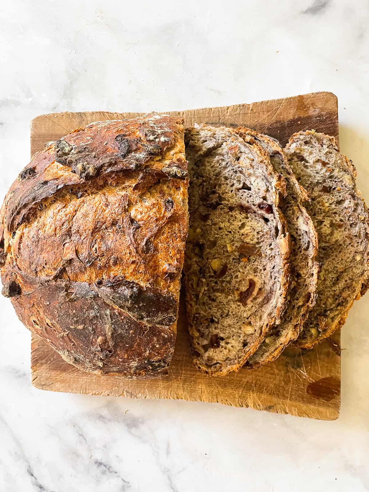This rustic no-knead gluten free cranberry and walnut bread is jam-packed with extras and features a beautiful, gluten-free crumb. A gluten free no knead cranberry bread cut into slices on a wooden cutting board.