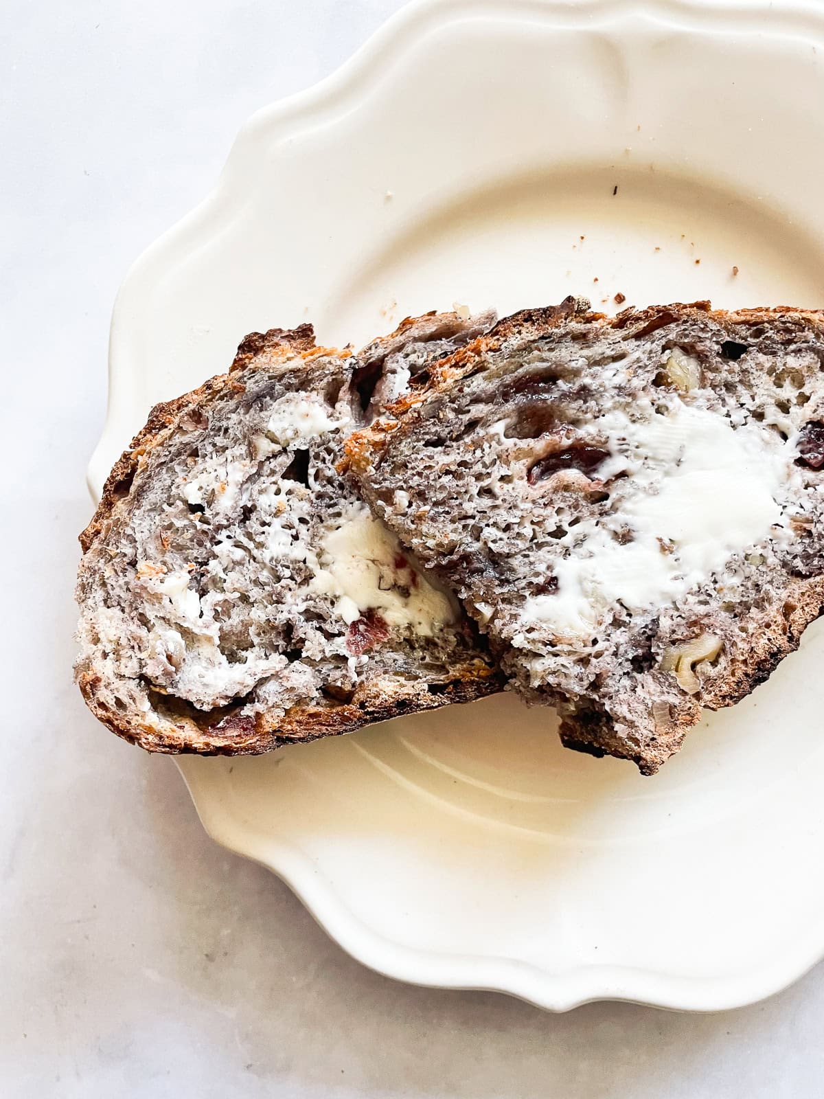 This rustic no-knead gluten free cranberry and walnut bread is jam-packed with extras and features a beautiful, gluten-free crumb. Slices of gluten free no knead cranberry walnut bread spread with butter.