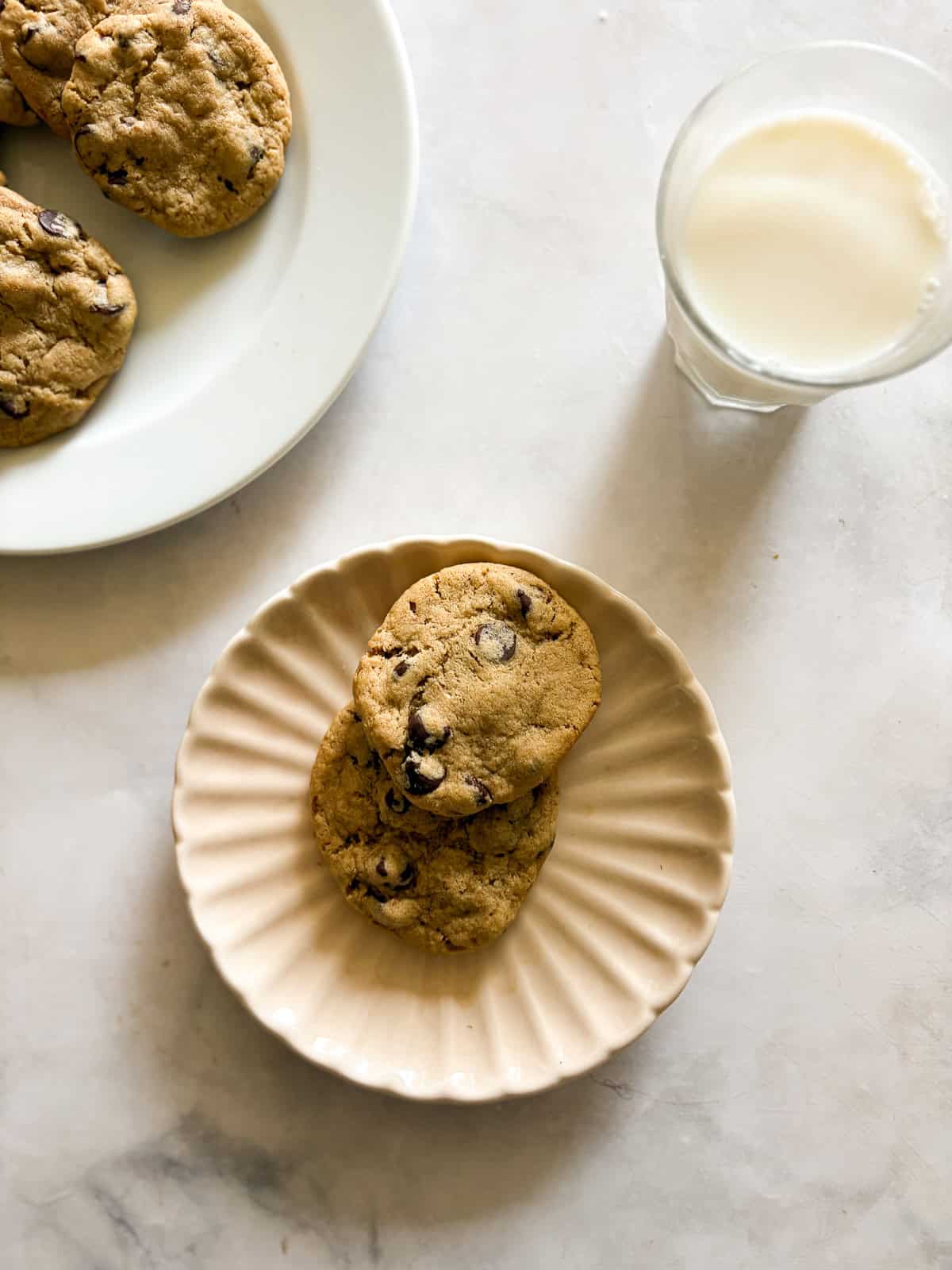 Chewy and irresistible, these gluten-free peanut butter chocolate chip cookies are made with plenty of creamy pb plus lots of chocolate! A couple of gluten free peanut butter chocolate chip cookies on a plate with a glass of milk.