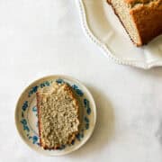 A slice of gluten free poppyseed bread on a plate next to the loaf.