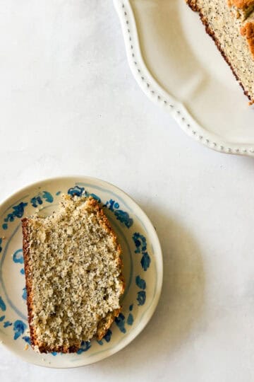 A slice of gluten free poppyseed bread on a plate next to the loaf.