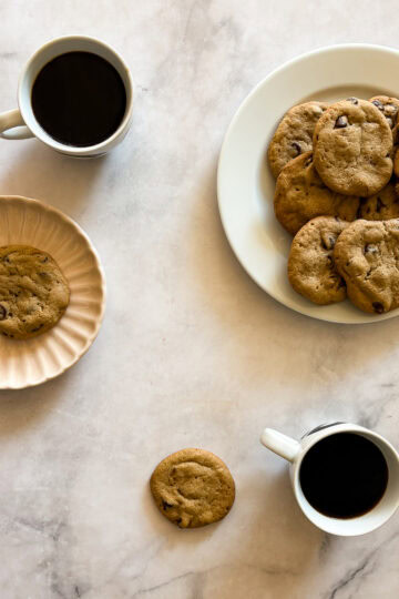 A plate of gluten free tahini chocolate chip cookies and cups of coffee.