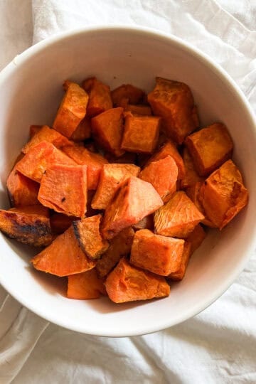 A bowl of baked sweet potato cubes placed on top of a white napkin.